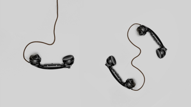 Zu sehen sind drei Telefonhörer. Ein Hörer hängt alleine an einem Kabel. Zwei Hörer sind durch ein kurzes Kabel miteinander verbunden.