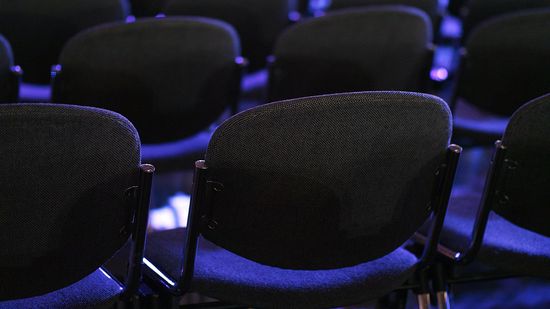 Zu sehen sind aufgereihte Stühle mit blauem Sitzpolster, von denen man hauptsächlich die Rücklehnen sieht.