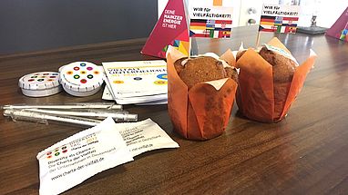 Auf einem Tisch stehen Muffins und verschiedene Give-aways der Charta der Vielfalt.