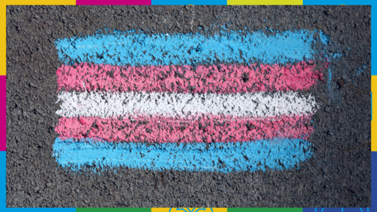 Zu sehen ist die trans-Flagge, mit Straßenkreide auf Asphalt gemalt