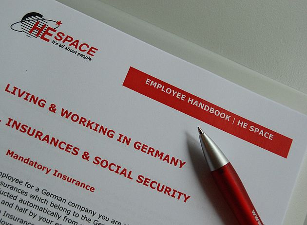 Ein Dokument mit der Aufschrift " Employee Handbook" von HESpace und ein Kugelschreiber.