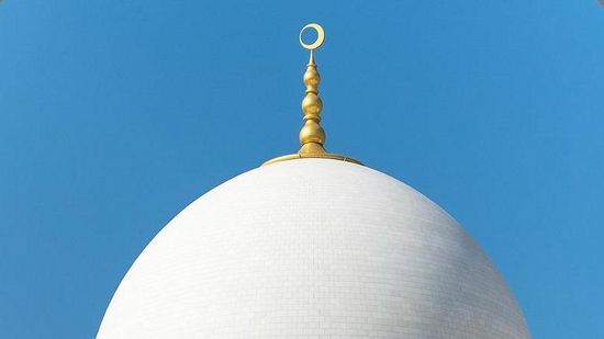 Zu sehen ist die weiße Kuppel einer Moschee vor blauem Himmel