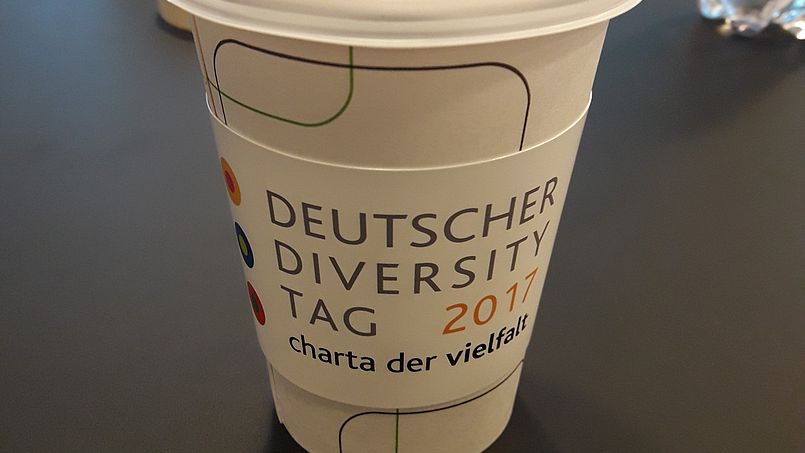 Ein Kaffeebecher mit dem Logo des DDT17 steht auf einem Tisch.