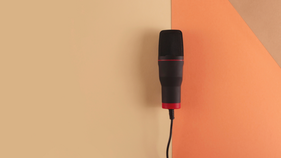 Zu sehen ist ein Mikrofon an einer Schnur vor orangenem Hintergrund.