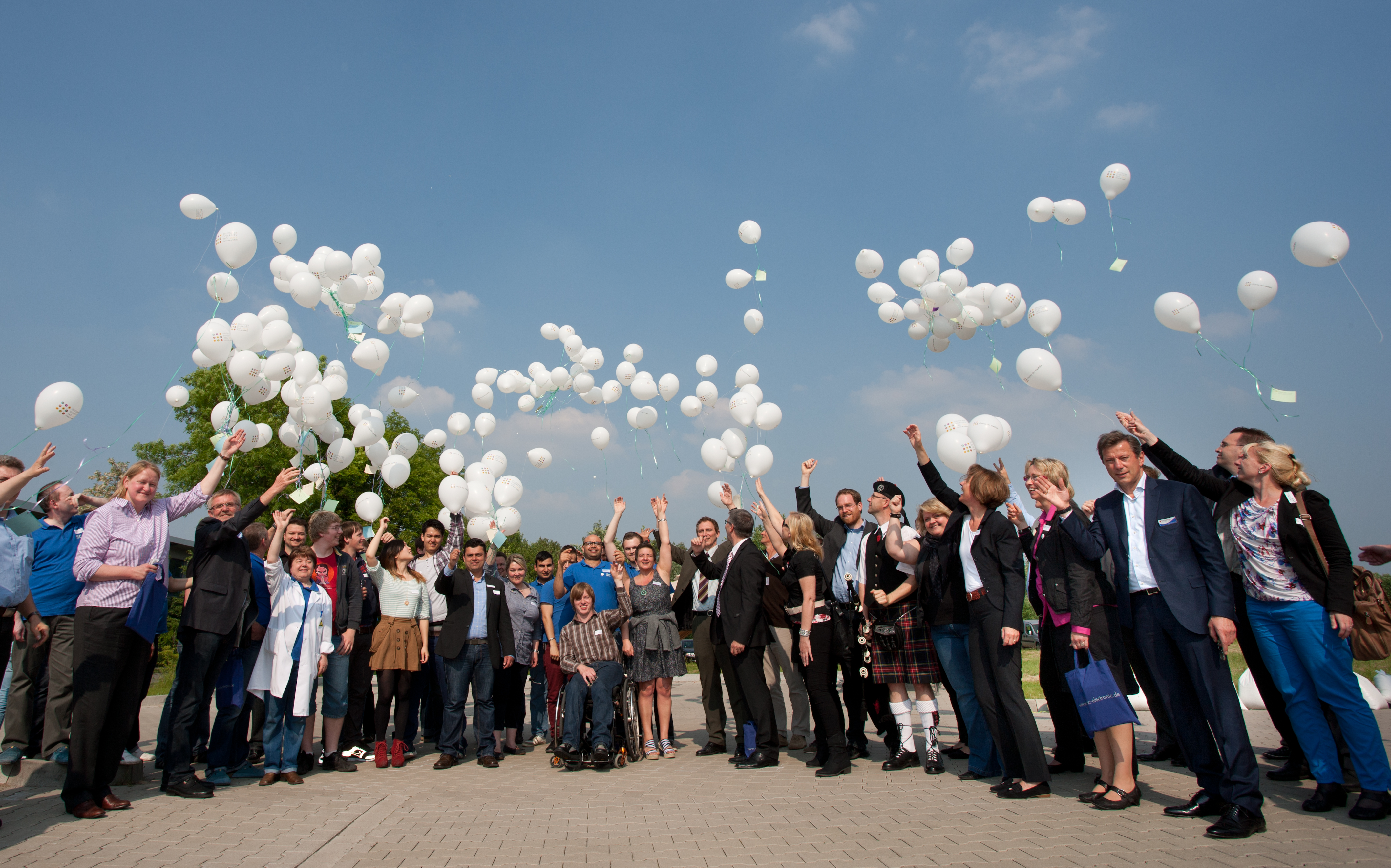 Eine größere Gruppe Menschen lässt Luftballons steigen.
